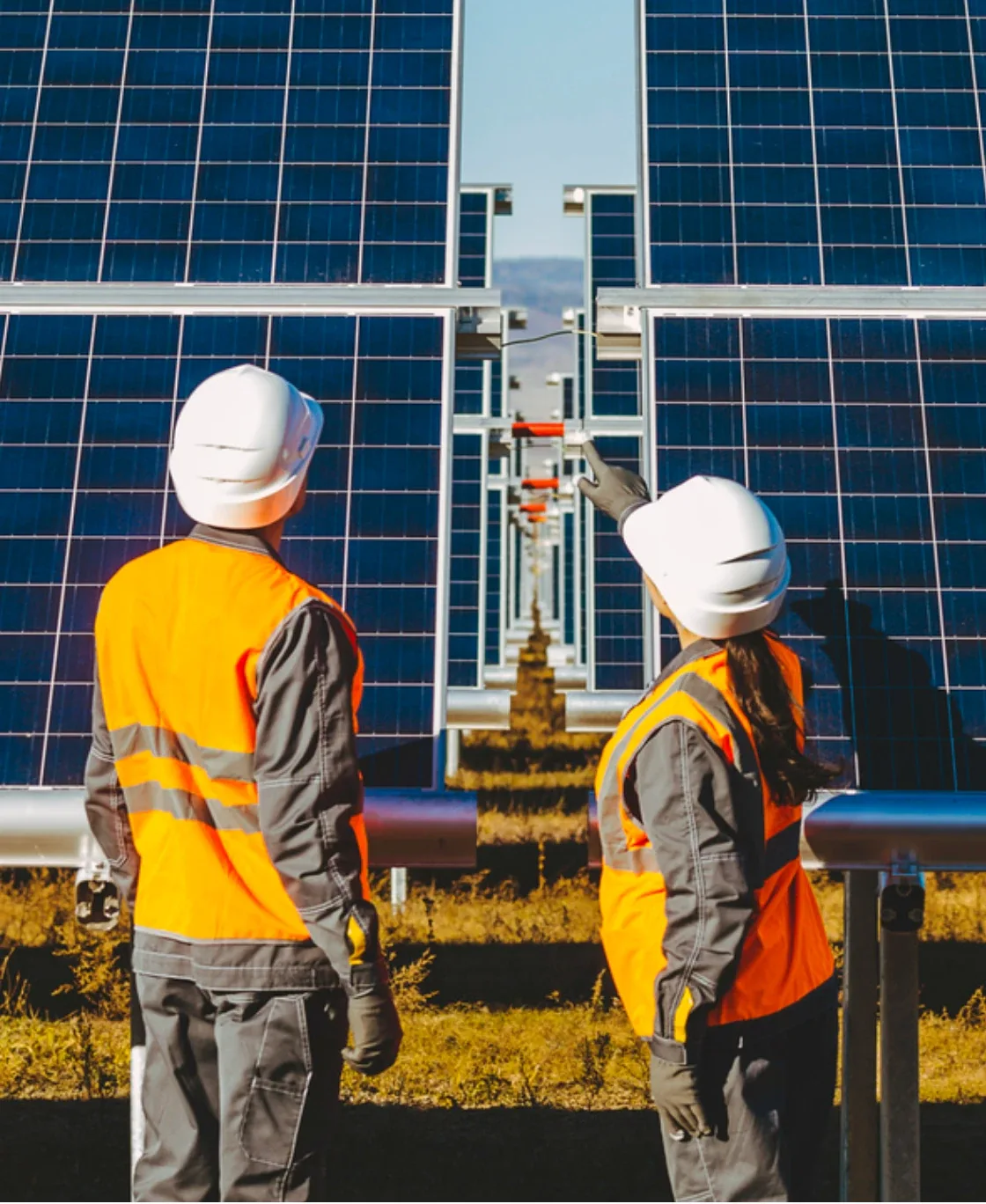 Two engineers in hard hats inspecting rows of solar panels