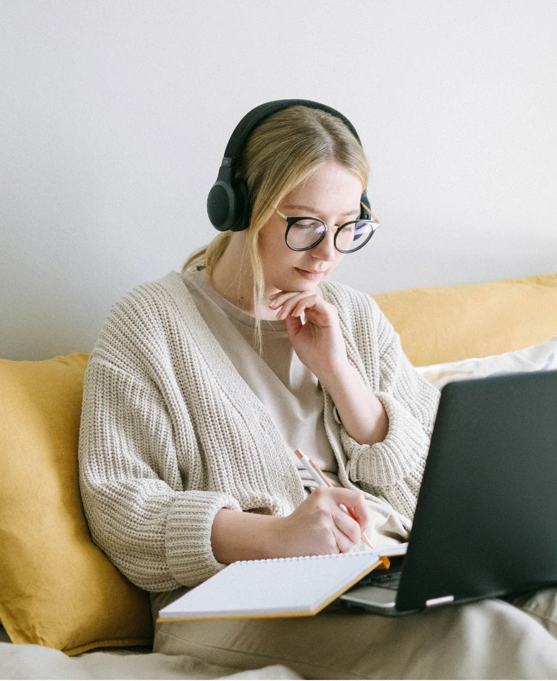 Woman with headphones taking notes during an online therapy session on her laptop