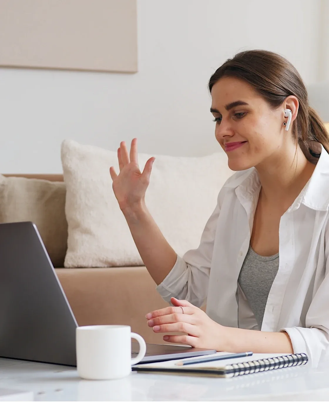 Smiling woman with earbuds talking during a video session on her laptop