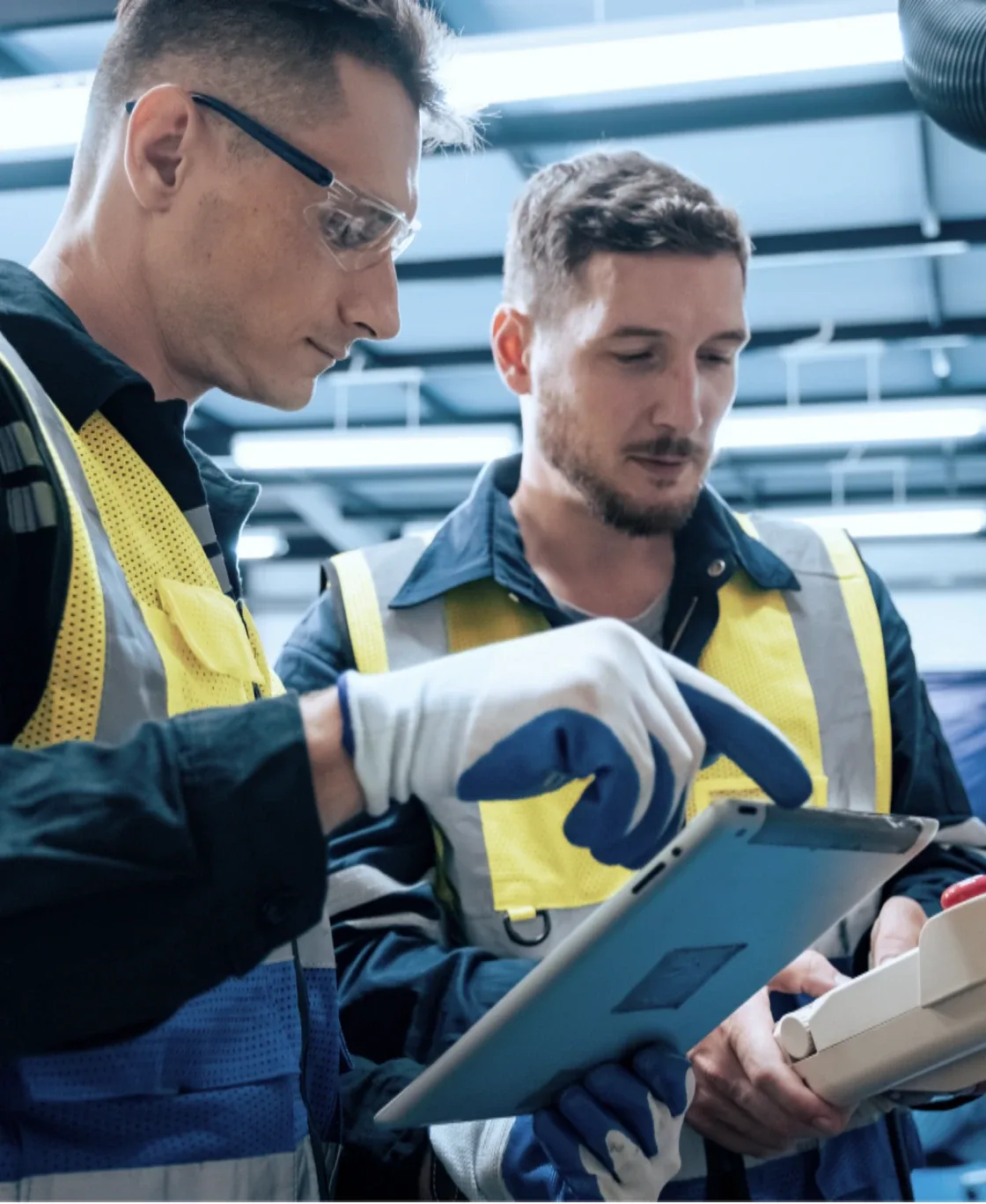 Two technicians in safety glasses inspecting a vehicle with a tablet