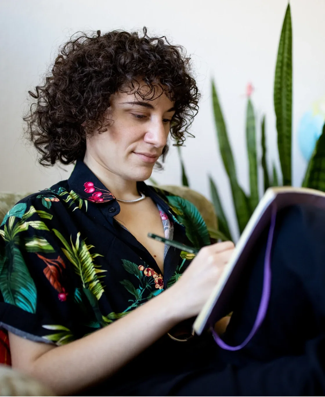 Woman writing in a notebook beside a plant