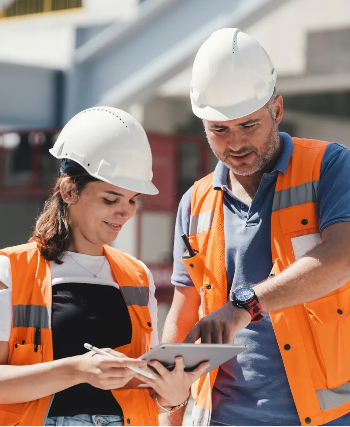 Two construction workers in hard hats reviewing a tablet on site