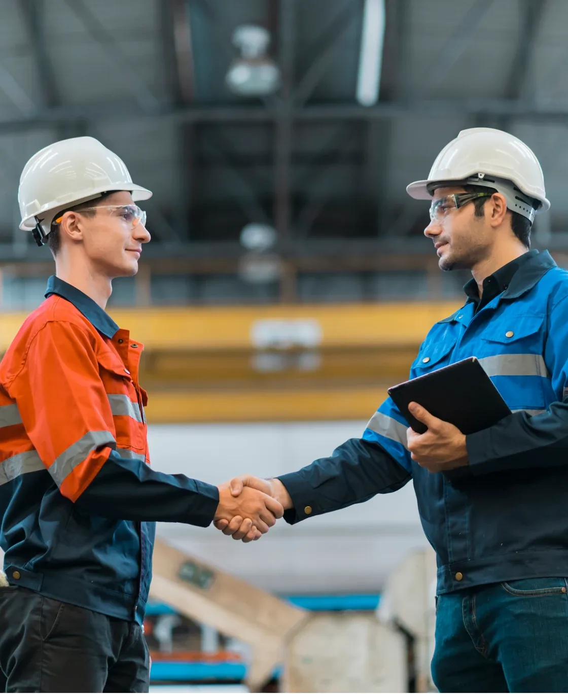 Two construction workers shaking hands in a warehouse