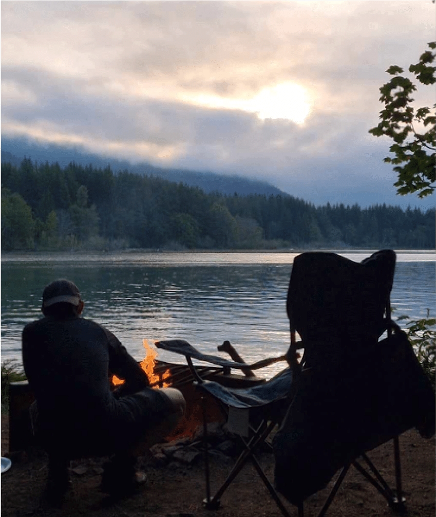 A man preparing dinner while camping in front of a lake